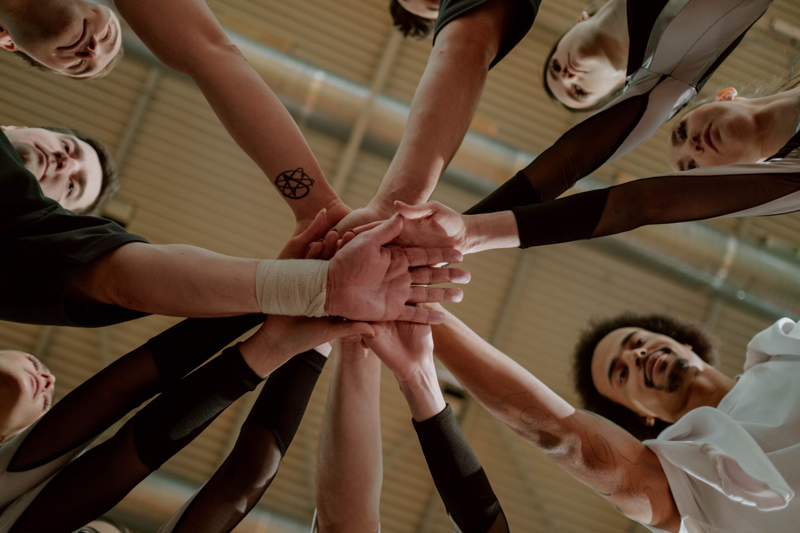 A diverse group of people joins hands in a supportive team gesture from a low angle.